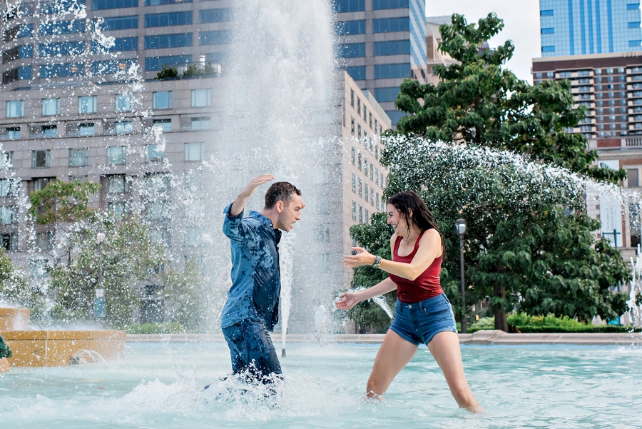 A man and woman have a fun water fight in Swann Memorial Fountain for their engagement session.
